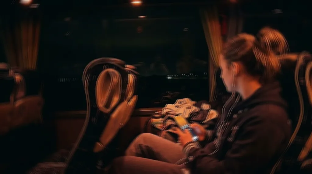 Athlete on a night bus ride, headphones on, checking their phone